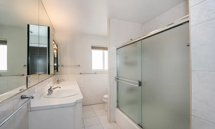 Full bathroom featuring vanity, bath / shower combo with glass door, tile patterned flooring, toilet, and tile walls