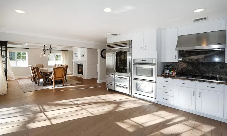 Kitchen featuring stainless steel appliances, crown molding, wall chimney range hood, hardwood / wood-style flooring, and white cabinetry