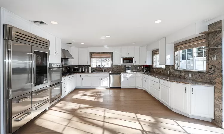 Kitchen with white cabinets, stainless steel appliances, light hardwood / wood-style flooring, and range hood