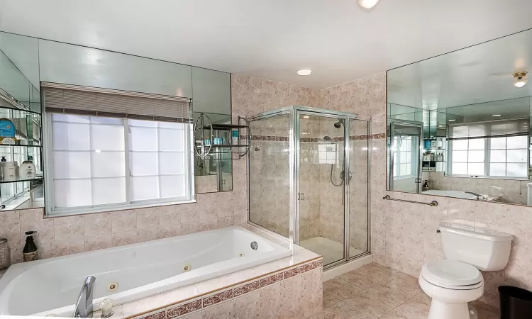 Bathroom with separate shower and tub, tile patterned floors, tile walls, and toilet