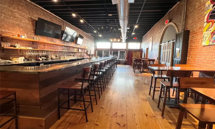 Bar with track lighting, light hardwood / wood-style flooring, and brick wall