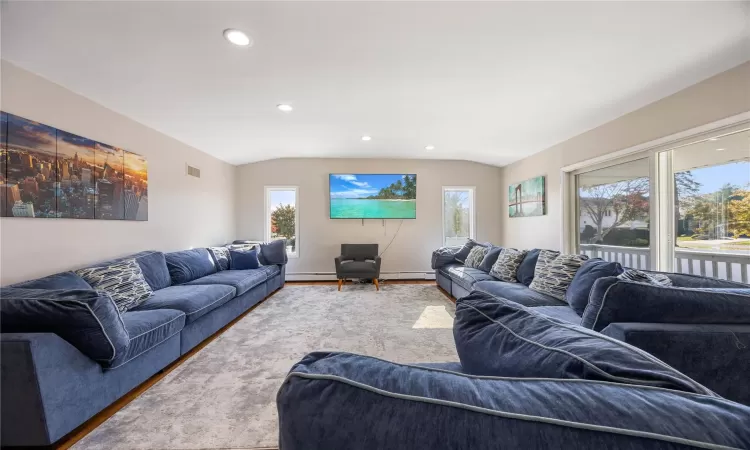 Living room with hardwood / wood-style flooring, a baseboard heating unit, and vaulted ceiling