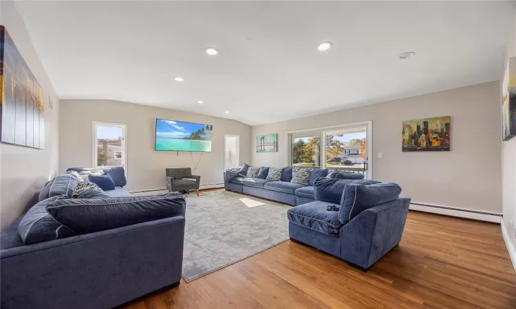 Living room featuring wood-type flooring, vaulted ceiling, and a baseboard heating unit