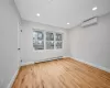 Empty room featuring baseboard heating, light wood-type flooring, and an AC wall unit