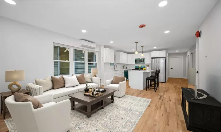 Living room with a wall mounted air conditioner, light wood-type flooring, and sink