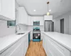 Kitchen featuring sink, hanging light fixtures, light wood-type flooring, white cabinetry, and stainless steel appliances