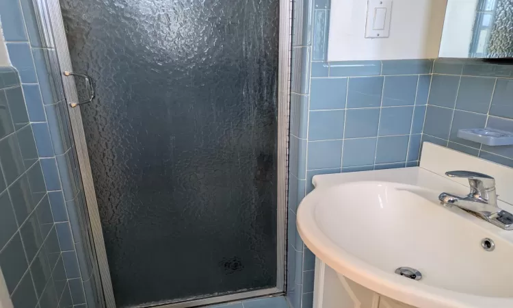 Bathroom featuring vanity, a shower with door, and tile walls