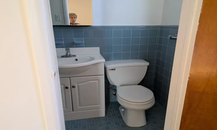 Bathroom featuring tile patterned flooring, vanity, toilet, and tile walls