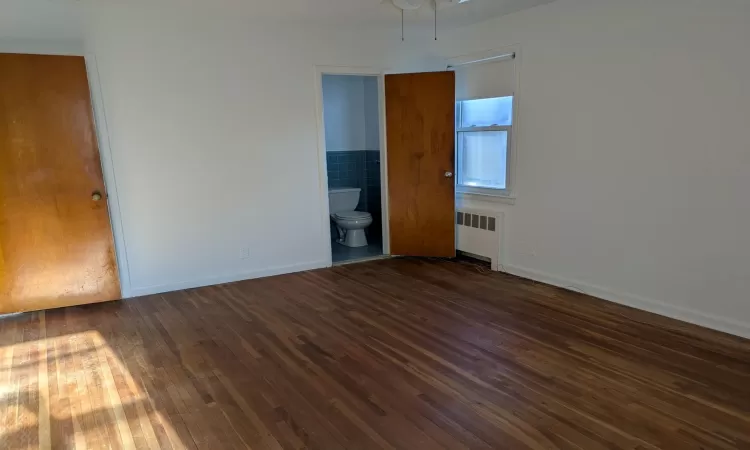 Empty room with ceiling fan, dark hardwood / wood-style flooring, and radiator