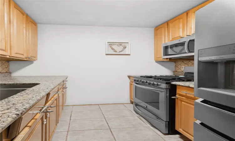 Kitchen with decorative backsplash, light tile patterned floors, stainless steel appliances, and light stone counters