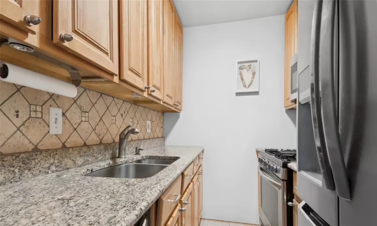 Kitchen with sink, stainless steel appliances, light stone counters, decorative backsplash, and light tile patterned flooring