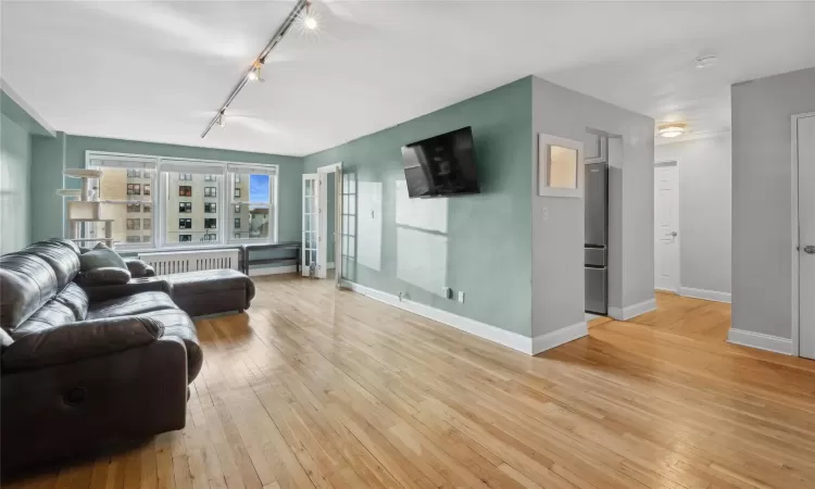 Living room featuring light wood-type flooring, track lighting, and radiator