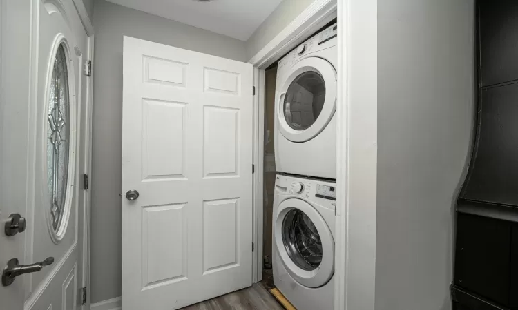 Clothes washing area with dark hardwood / wood-style flooring and stacked washer and dryer