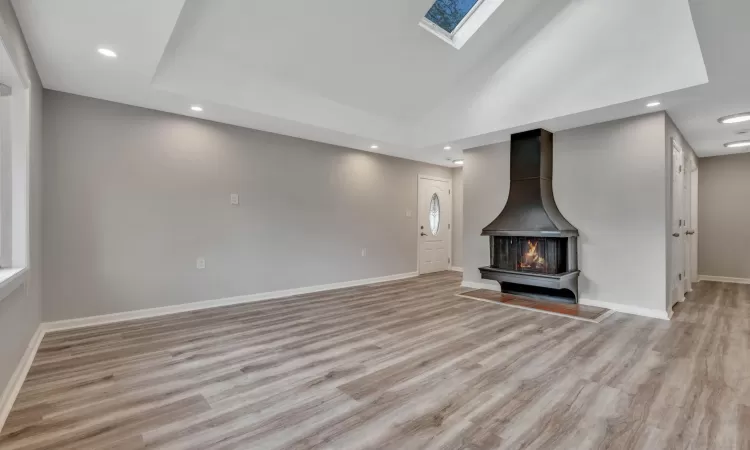 Unfurnished living room with a wood stove, a skylight, and light hardwood / wood-style floors