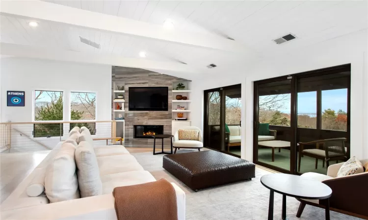 Living room with vaulted ceiling with beams, built in features, and a fireplace