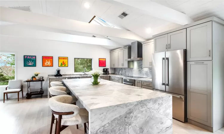 Kitchen featuring gray cabinetry, a wealth of natural light, wall chimney range hood, and high quality fridge