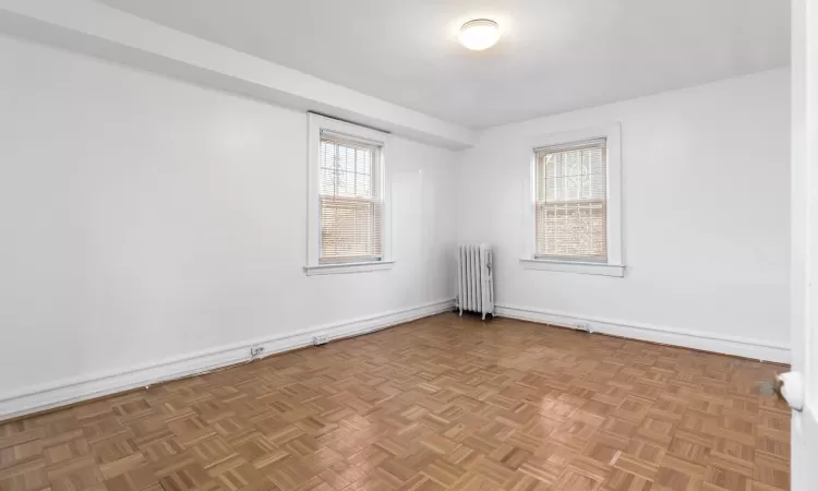 Unfurnished room featuring radiator heating unit, light parquet flooring, and a healthy amount of sunlight