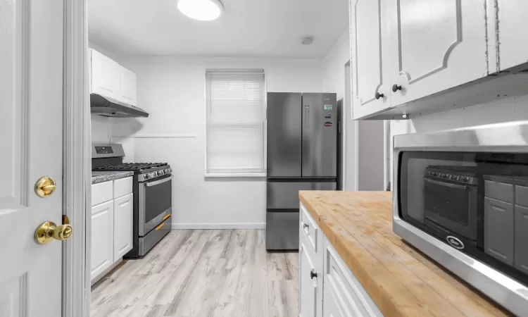 Kitchen with light hardwood / wood-style flooring, white cabinets, stainless steel appliances, and wood counters