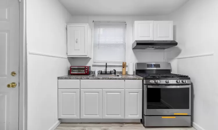 Kitchen featuring sink, stainless steel gas stove, white cabinets, and ventilation hood