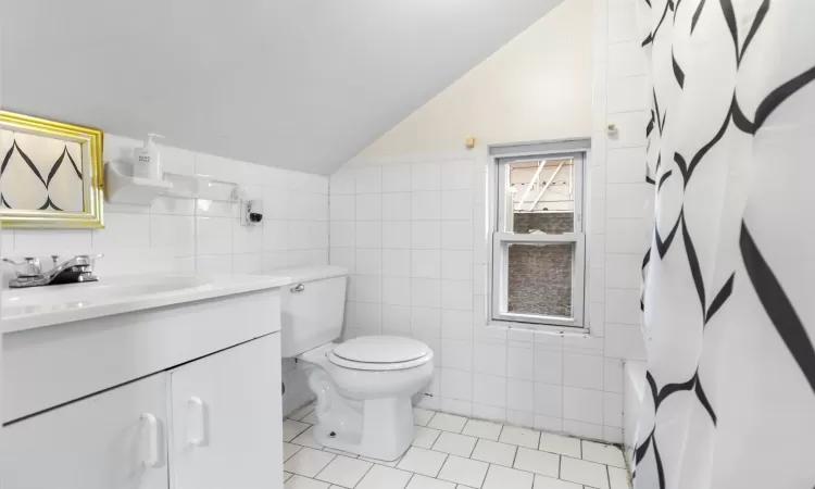 Full bathroom featuring tile patterned floors, lofted ceiling, vanity, and tile walls