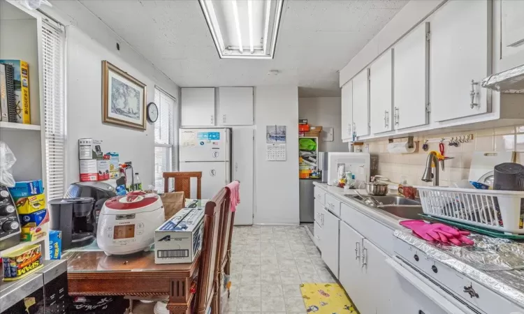 Kitchen with sink, tasteful backsplash, range hood, white appliances, and white cabinets