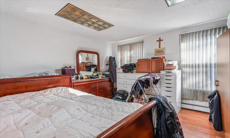 Bedroom featuring a textured ceiling, a baseboard radiator, and light hardwood / wood-style floors