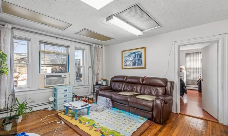 Living room featuring a textured ceiling, cooling unit, a baseboard heating unit, and hardwood / wood-style flooring