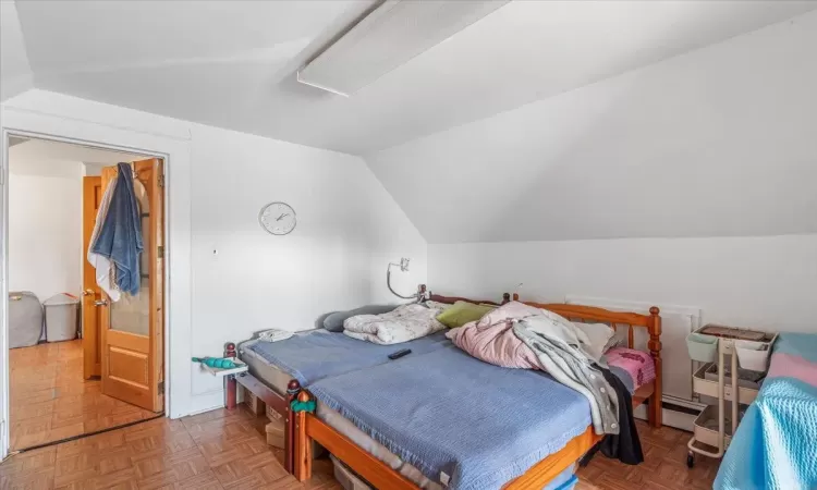 Bedroom featuring parquet floors, a baseboard radiator, and vaulted ceiling