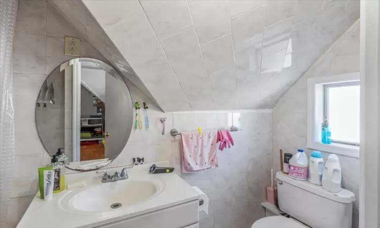 Bathroom featuring vanity, tile walls, and toilet