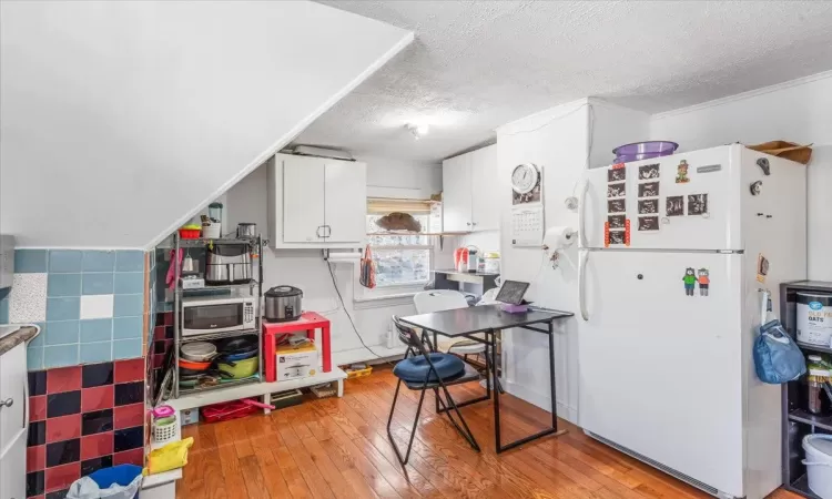 Kitchen featuring a textured ceiling, white appliances, tile walls, white cabinets, and light hardwood / wood-style floors