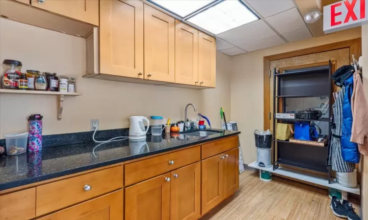 Kitchen featuring a paneled ceiling, light hardwood / wood-style flooring, dark stone counters, and sink