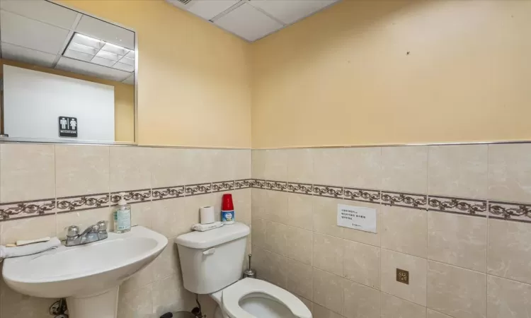 Bathroom featuring a paneled ceiling, toilet, sink, and tile walls