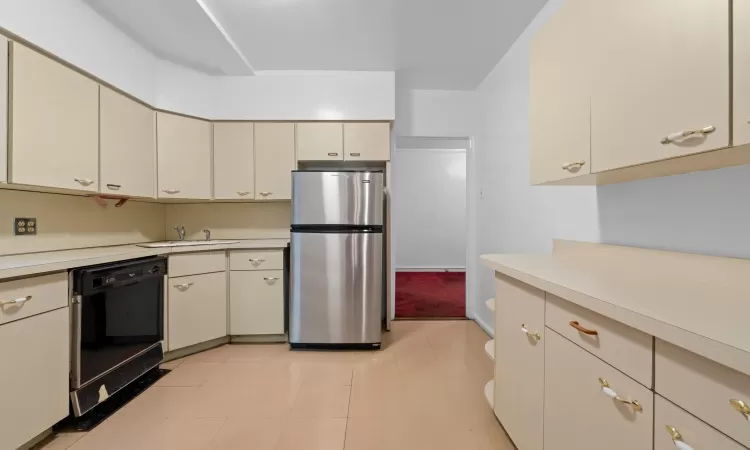 Kitchen with stainless steel refrigerator, white gas range, sink, black dishwasher, and cream cabinetry