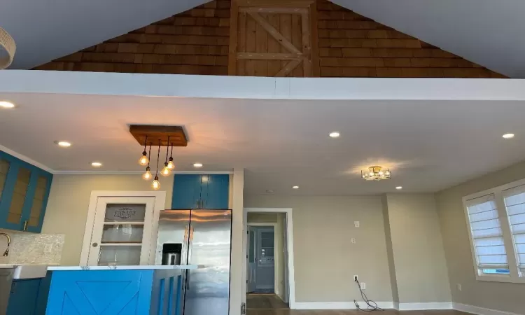 Kitchen with high vaulted ceiling, decorative light fixtures, stainless steel refrigerator with ice dispenser, and blue cabinets