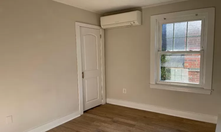 Spare room with a wall mounted air conditioner, crown molding, and dark wood-type flooring