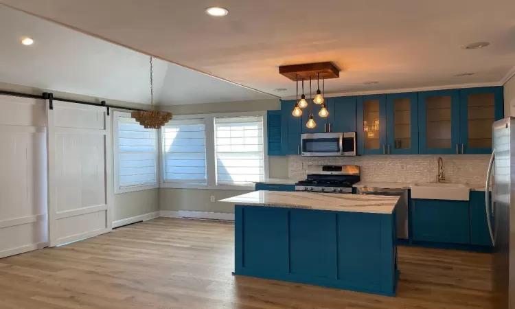 Kitchen with blue cabinetry, sink, stainless steel appliances, a barn door, and decorative light fixtures