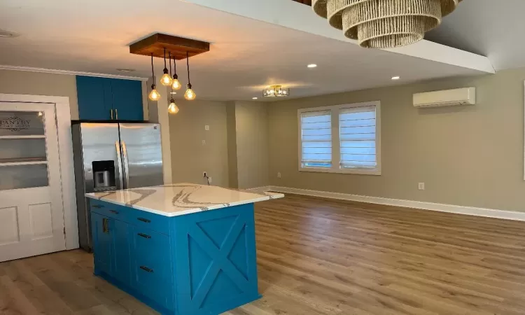 Kitchen with a center island, dark wood-type flooring, an AC wall unit, hanging light fixtures, and blue cabinetry