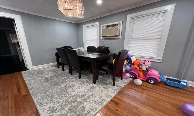 Dining area featuring an AC wall unit, hardwood / wood-style floors, a chandelier, and ornamental molding