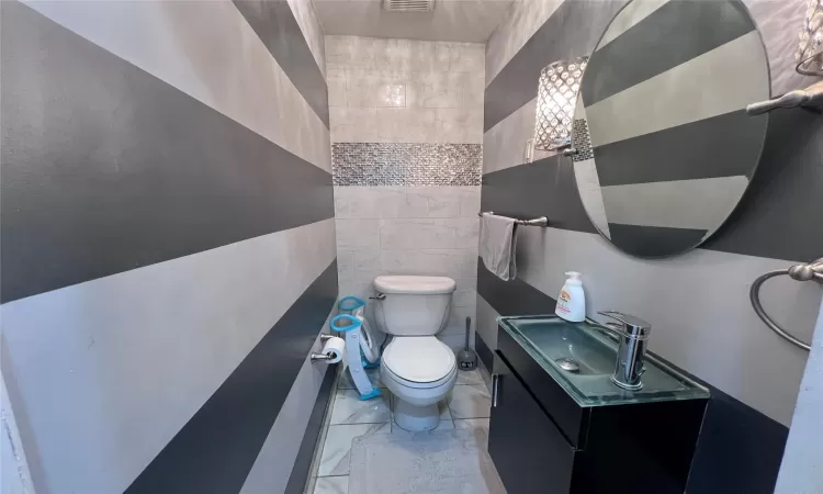 Bathroom featuring vanity, tile walls, and toilet