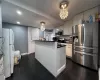 Kitchen featuring a kitchen island with sink, an inviting chandelier, hanging light fixtures, appliances with stainless steel finishes, and white cabinetry