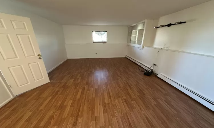 Empty room featuring baseboard heating and dark wood-type flooring