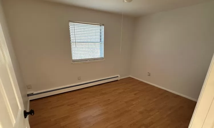 Empty room featuring baseboard heating and dark wood-type flooring