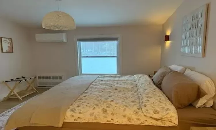 Bedroom featuring hardwood / wood-style floors, radiator heating unit, and a wall mounted air conditioner