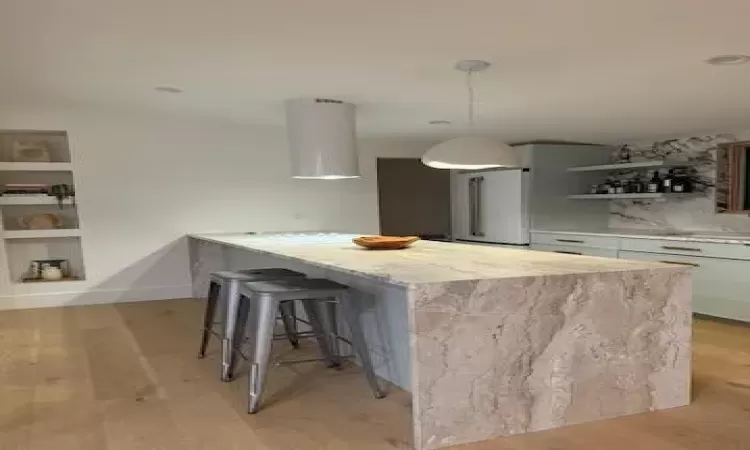 Kitchen with light hardwood / wood-style floors, a breakfast bar area, built in features, pendant lighting, and white cabinets