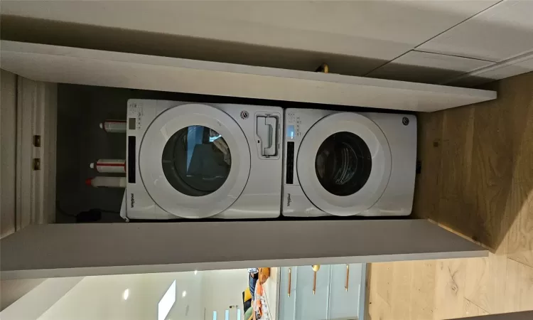 Laundry area featuring a skylight, stacked washing maching and dryer, and hardwood / wood-style flooring