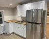 Kitchen with stainless steel refrigerator, sink, white cabinets, and wooden counters