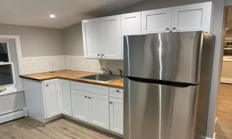 Kitchen with stainless steel refrigerator, sink, white cabinets, and wooden counters