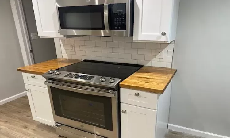 Kitchen featuring backsplash, white cabinets, light hardwood / wood-style flooring, appliances with stainless steel finishes, and butcher block countertops