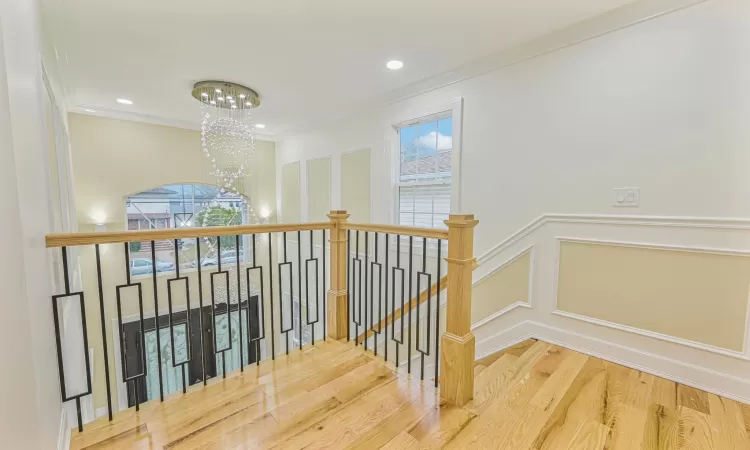 Stairs featuring plenty of natural light, wood-type flooring, crown molding, and a chandelier