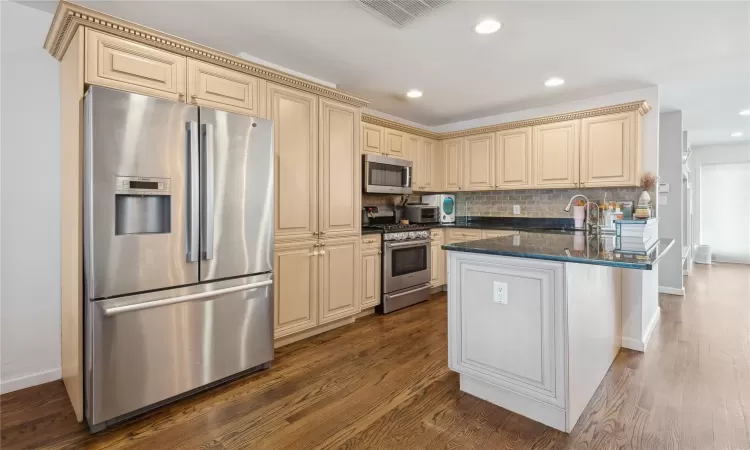 Kitchen featuring backsplash, dark hardwood / wood-style flooring, dark stone counters, and appliances with stainless steel finishes